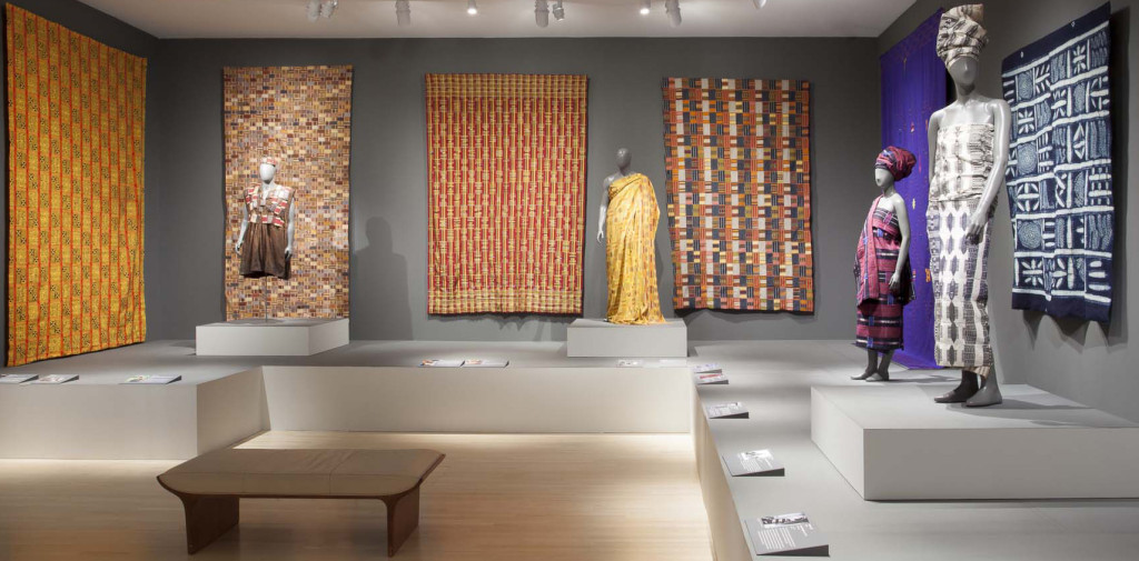 Gallery installation of 'Majestic African Textiles' at Indianapolis Museum of Art showing various Ewe and Kente narrow strip woven cloths, alongside Cameroonian and Nigerian cloths