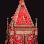 Sitr (or sitarah) for the mahmal, bearing the tughra of Sultan Abdülaziz, presented by Isma‘il Pasha, the khedive of Egypt Ottoman Egypt, Cairo, 1867-76; red silk with green silk appliqués, embroidered in silver and silver-gilt wire over cotton and silk thread padding; with contemporary banners and copper-alloy finials, and a wooden frame, probably contemporary 400 (approx. height assembled) x 130 x 102 cm